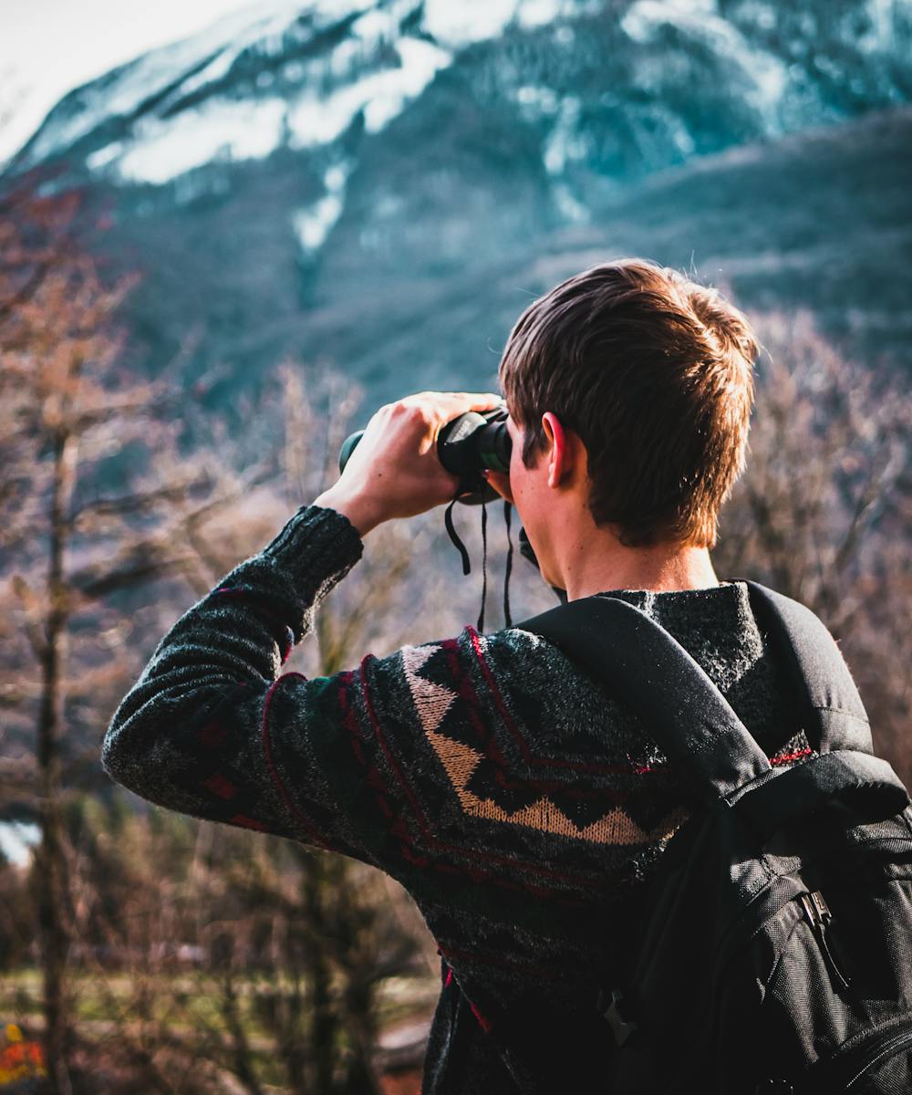 Person mit Fernglas beim Beobachten einer Berglandschaft